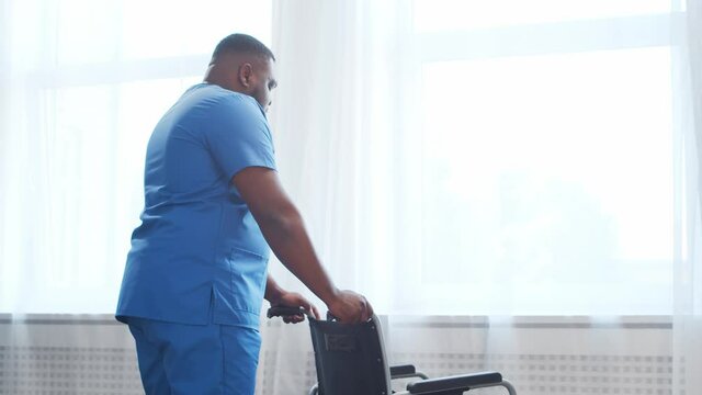 African-American caregiver and an empty wheelchair. Professional nurse in a nursing home. Assistance, rehabilitation and health care.