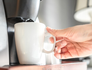 Woman using coffee maker, brewing hot beverage in the morning with blurred background. Automatic coffee machine at snack bar in hotel room. Person making caffeine drink at an office.