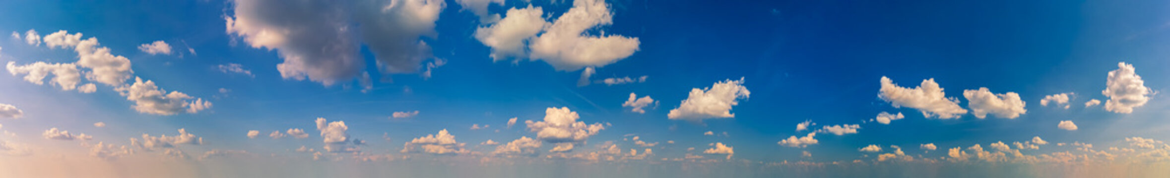 Wide panorama of blue sky with fluffy white clouds in the late afternoon.