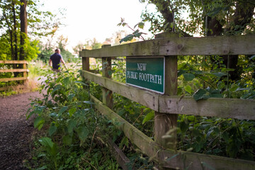 Close-up, shallow focus of a New Public Footpath seen seen at the entrance to a copse area in a rural forest. A walker can be seen in the path.