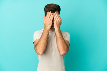 Young caucasian handsome man isolated on blue background covering eyes by hands