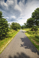 idyllic road through the fields against cloudy sky
