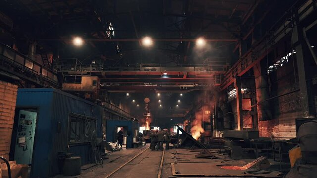 Steel production at metallurgical plant, large workshop with beam cranes and underground blast furnace.