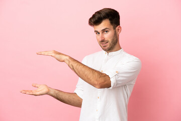 Young caucasian handsome man isolated on pink background holding copyspace to insert an ad