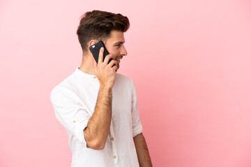 Young caucasian handsome man isolated on pink background keeping a conversation with the mobile phone with someone