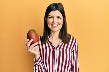 Young hispanic woman holding mango looking positive and happy standing and smiling with a confident smile showing teeth