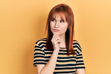 Redhead young woman wearing casual striped t shirt thinking concentrated about doubt with finger on chin and looking up wondering