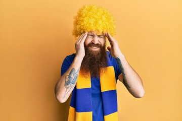 Redhead man with long beard football hooligan cheering game wearing funny wig with hand on head for...