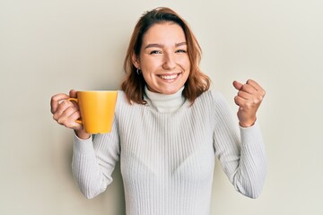 Young caucasian woman holding coffee screaming proud, celebrating victory and success very excited with raised arm