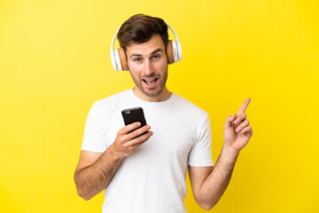 Young caucasian handsome man isolated on yellow background listening music with a mobile and singing