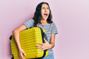 Hispanic teenager girl with dental braces holding cabin bag angry and mad screaming frustrated and...