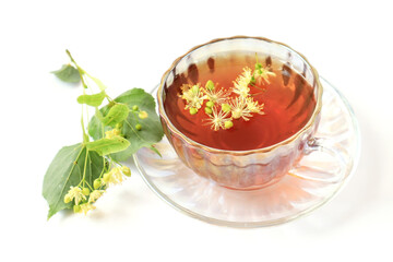 The concept of taking medicinal herbal teas.A cup of tea on a saucer with linden flowers , green branches on a light background, close-up.