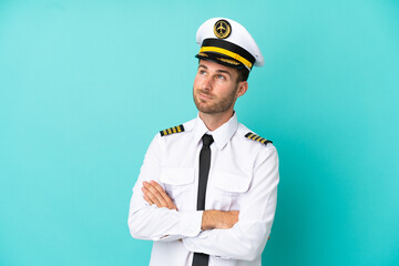 Airplane caucasian pilot isolated on blue background looking up while smiling © luismolinero