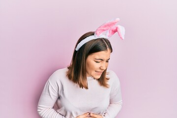 Obraz na płótnie Canvas Young beautiful woman wearing cute easter bunny ears with hand on stomach because nausea, painful disease feeling unwell. ache concept.