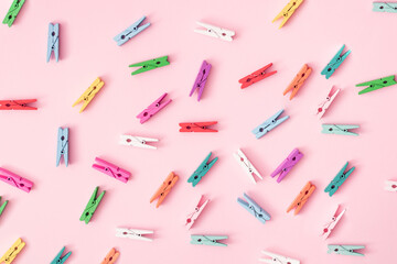 Small colorful wooden laundry tongs arranged on a pink background.