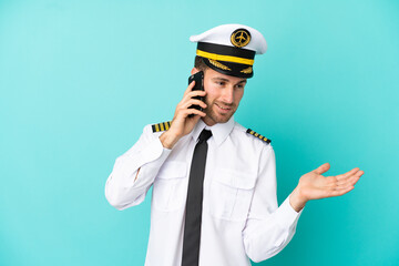 Airplane caucasian pilot isolated on blue background keeping a conversation with the mobile phone with someone