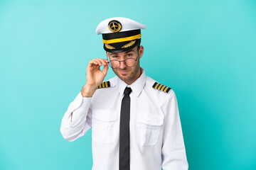 Airplane caucasian pilot isolated on blue background with glasses and happy
