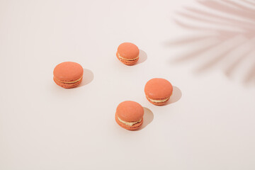 Pink macarons with a white cream on a light background and a shade of palm trees.