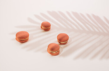 Pink macarons with a white cream on a light background and a shade of palm trees.