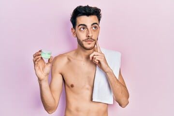 Fototapeta premium Young hispanic man shirtless wearing towel and eye bags patches serious face thinking about question with hand on chin, thoughtful about confusing idea