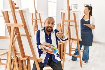 Senior artist man at art studio pointing fingers to camera with happy and funny face. good energy and vibes.