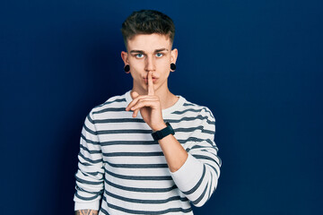 Young caucasian boy with ears dilation wearing casual striped shirt asking to be quiet with finger on lips. silence and secret concept.