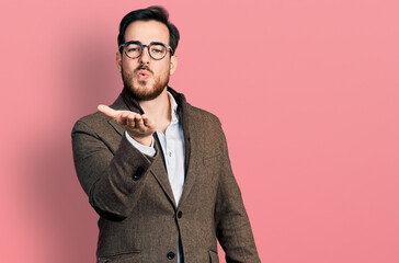 Young hispanic man wearing business jacket and glasses looking at the camera blowing a kiss with...