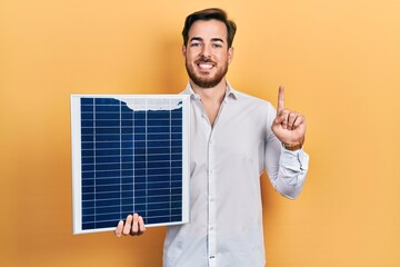Handsome caucasian man with beard holding photovoltaic solar panel smiling with an idea or question...