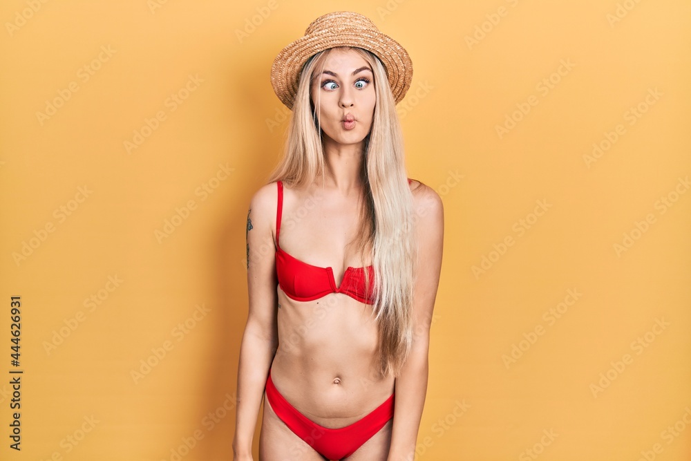 Wall mural young caucasian woman wearing bikini and summer hat making fish face with lips, crazy and comical ge