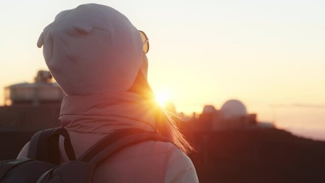 Woman looking at observatory on mountain in golden sunset, thinking about life