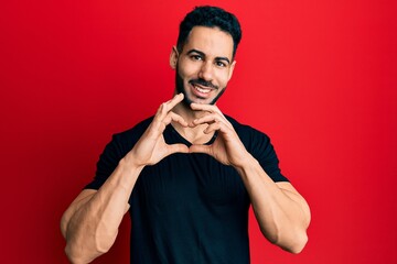 Fototapeta na wymiar Young hispanic man wearing casual black t shirt smiling in love doing heart symbol shape with hands. romantic concept.