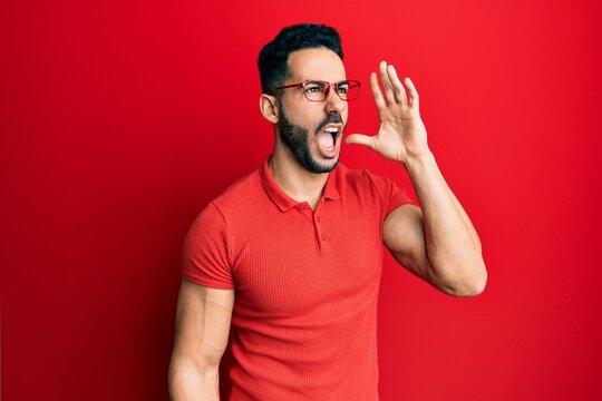 Young hispanic man wearing casual clothes and glasses shouting and screaming loud to side with hand on mouth. communication concept.