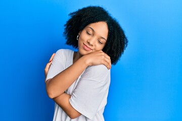 Young african american girl wearing casual white t shirt hugging oneself happy and positive, smiling confident. self love and self care