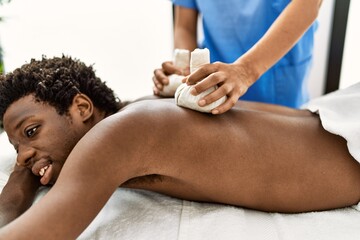 Young african american man reciving herbal pouches thai massage at beauty center.