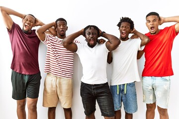 Young african group of friends standing together over isolated background crazy and scared with hands on head, afraid and surprised of shock with open mouth