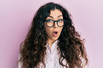 Obraz premium Young brunette woman with curly hair wearing casual clothes and glasses afraid and shocked with surprise expression, fear and excited face.