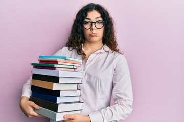 Young brunette woman with curly hair holding a pile of books depressed and worry for distress, crying angry and afraid. sad expression.