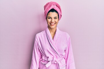Young hispanic woman wearing shower towel cap and bathrobe with a happy and cool smile on face....