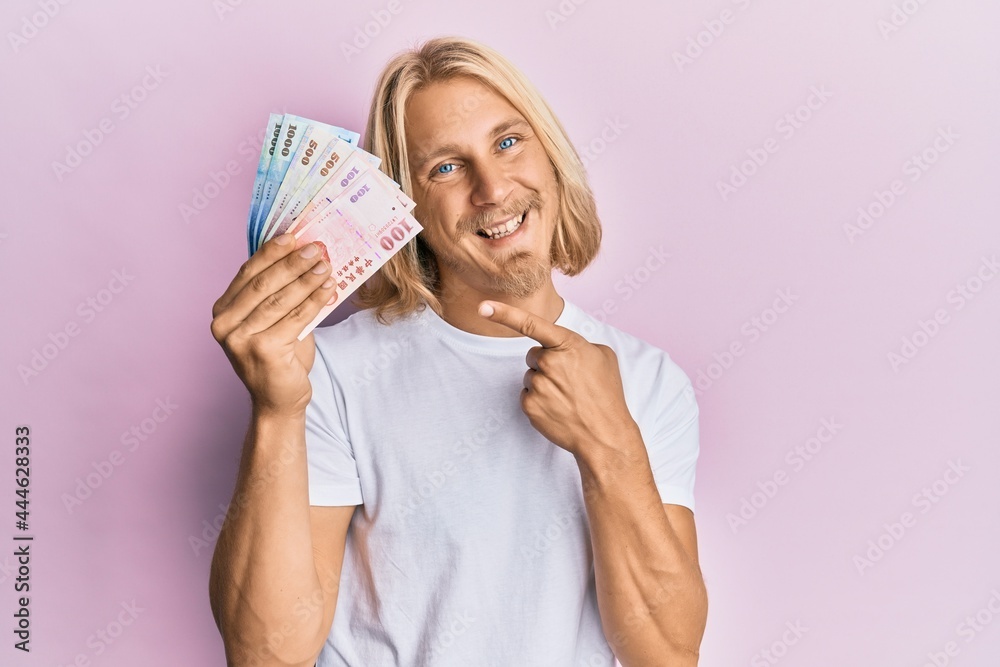 Sticker caucasian young man with long hair holding new taiwan dollars banknotes smiling happy pointing with 