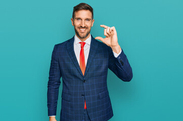 Handsome man with beard wearing business suit and tie smiling and confident gesturing with hand doing small size sign with fingers looking and the camera. measure concept.