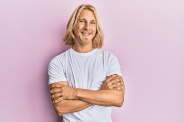 Caucasian young man with long hair wearing casual white t shirt happy face smiling with crossed arms looking at the camera. positive person.