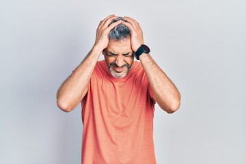 Handsome middle age man with grey hair wearing casual t shirt suffering from headache desperate and stressed because pain and migraine. hands on head.