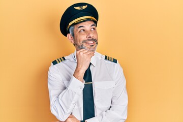 Handsome middle age man with grey hair wearing airplane pilot uniform with hand on chin thinking about question, pensive expression. smiling and thoughtful face. doubt concept.