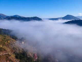 Aerial view of Itaipava, Petrópolis. Early morning with a lot of fog in the city. Mountains with blue sky and clouds around Petrópolis, mountainous region of Rio de Janeiro, Brazil. Drone photo. 
