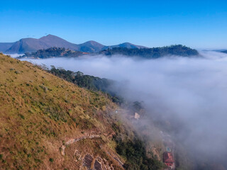 Aerial view of Itaipava, Petrópolis. Early morning with a lot of fog in the city. Mountains with blue sky and clouds around Petrópolis, mountainous region of Rio de Janeiro, Brazil. Drone photo. 
