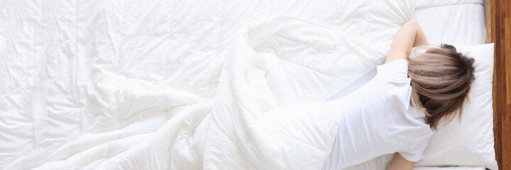 Fototapeta premium Woman lying on white bed and holding bottle with alcohol in hand
