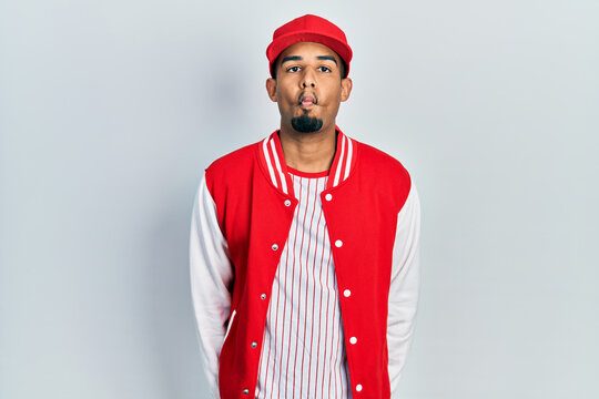 Young african american man wearing baseball uniform making fish face with lips, crazy and comical gesture. funny expression.