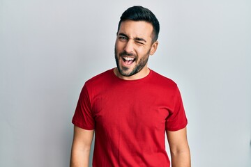Young hispanic man wearing casual clothes winking looking at the camera with sexy expression,...