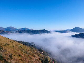 Aerial view of Itaipava, Petrópolis. Early morning with a lot of fog in the city. Mountains with blue sky and clouds around Petrópolis, mountainous region of Rio de Janeiro, Brazil. Drone photo. 