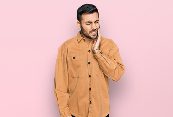 Young hispanic man wearing casual clothes touching mouth with hand with painful expression because of toothache or dental illness on teeth. dentist